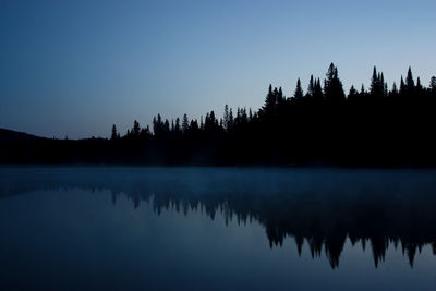 Reflection of silhouette trees in lake against blue sky