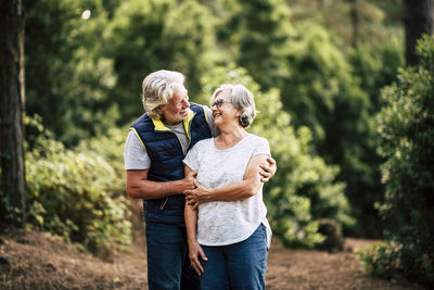 Smiling senior couple standing on land against trees in forest