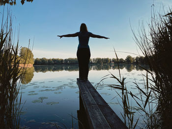 Rear view of woman standing by lake against sky