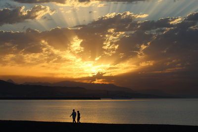 Silhouette people on sea against sky during sunset