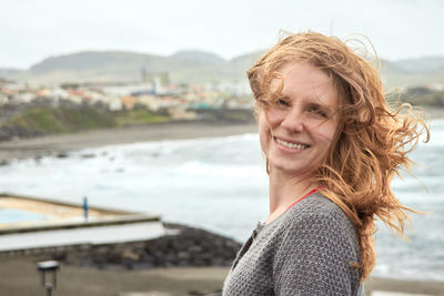 Portrait of smiling woman with tousled hair standing against sea