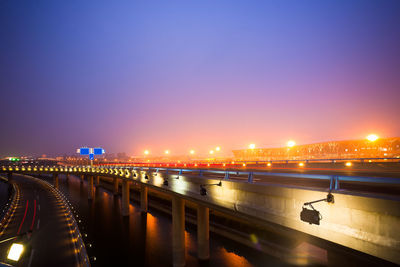 Illuminated bridge over river against sky at night