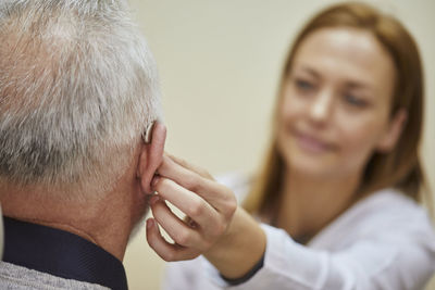 Female doctor applying hearing aid to senior man's ear