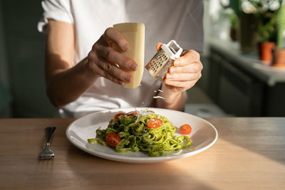 Woman hands grating parmesan cheese in pasta with sauce pesto, fresh cherry tomatoes. 