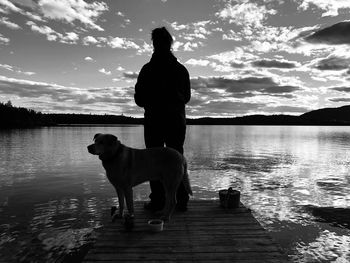 Silhouette man with dog on lake against sky