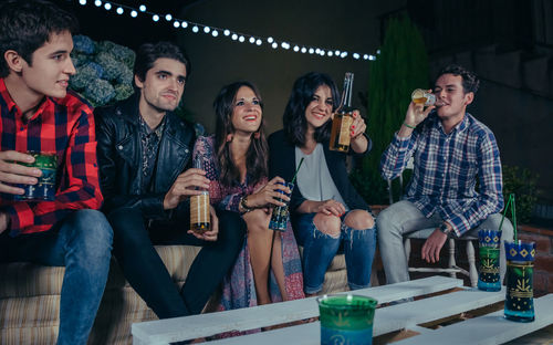 Friends having drinks while sitting at patio during night