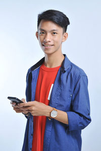 Potrait of handsome young asian man holding a smart phone and wear wristwatch with pretty smiling look at the camera