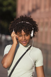  woman with curly hair listening to music on smartphone wears earphones in the street