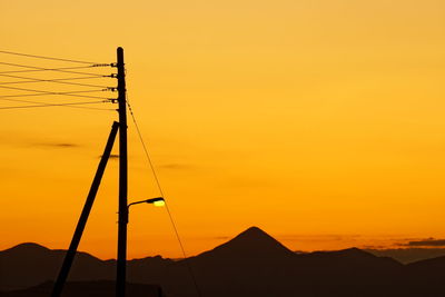 Silhouette electricity pylons against orange sky