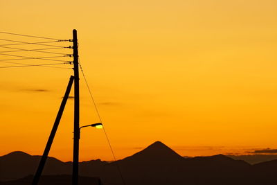 Silhouette electricity pylons against orange sky