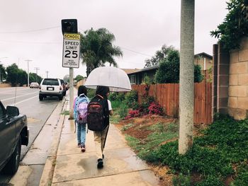 Rear view of people walking on road in rainy season