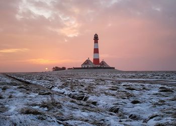 Lighthouse by sea against sky during sunset