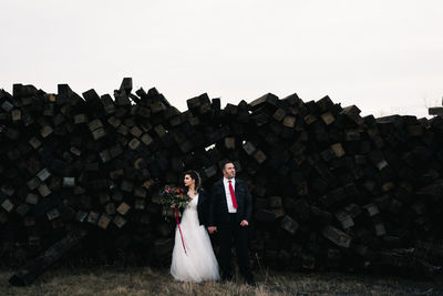 People standing by logs against clear sky