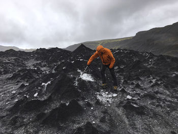 Man breaking ice on mountain against cloudy sky