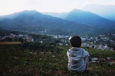 Rear view of man looking at cityscape against mountains