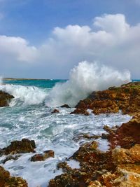 Waves splashing on rocks by sea against sky