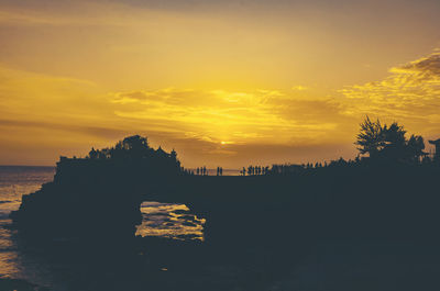 Silhouette trees by sea against orange sky