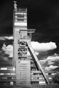 Low angle view of crane by building against sky