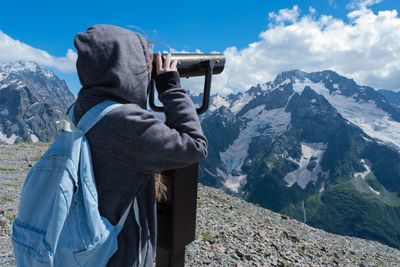 Girl looking at mountains with binoculars against sky