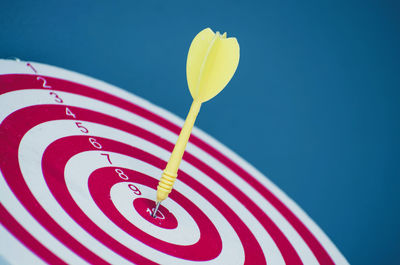 Close-up of dart stuck in board against blue background