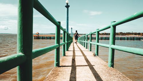 Rear view of man walking on footbridge over sea
