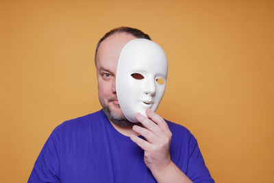 Portrait of man wearing mask against wall against orange background