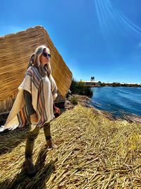 Side view of woman standing by lake against sky