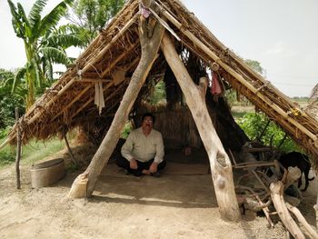 Portrait of young man sitting on wood against trees