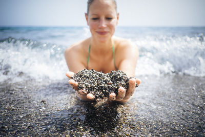 Woman holding wet black sand on seashore
