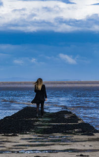 Rear view of woman standing at beach against blue sky