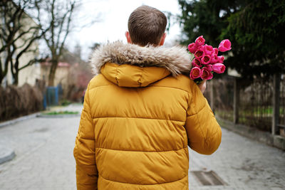 Blond man in a yellow winter jacket with a bouquet of tulips in hands