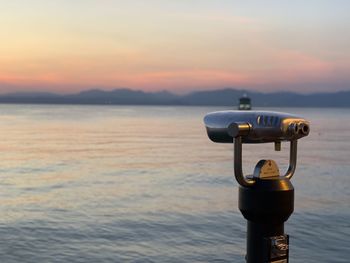 Close-up of coin-operated binoculars by sea against sky during sunset