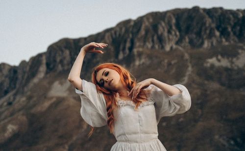 Young woman with arms raised standing against mountain