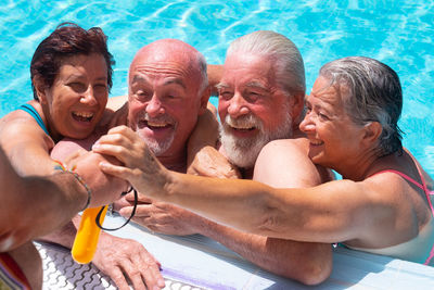 High angle view of happy friends holding person hand while swimming in pool