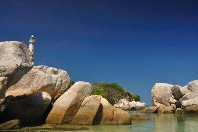 Rocks by sea against clear blue sky