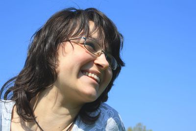 Low angle view of smiling young woman against clear blue sky