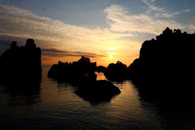 Silhouette rocks in sea against sky during sunset