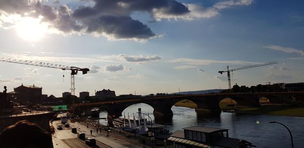 Bridge over river in city against sky at sunset