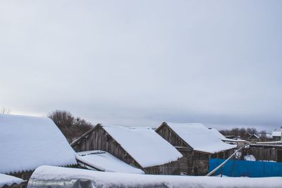 Snow covered houses by building against sky