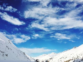 Low angle view of snowcapped mountains against blue sky