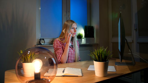 Side view of young woman sitting on table at home