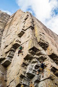 Low angle view of men climbing on rock against sky