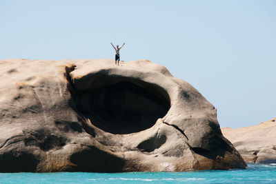 Man standing on rock by sea against clear sky