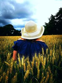 Rear view of woman in field against cloudy sky