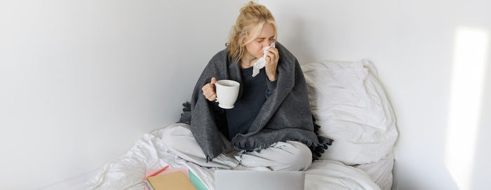 Portrait of young woman using digital tablet while sitting on bed at home