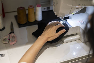 Woman is sewing black beanie hat on a sewing machine, using a sewing machine on the sewing table