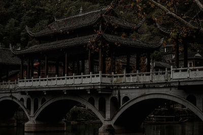 Low angle view of bridge over river amidst trees and buildings