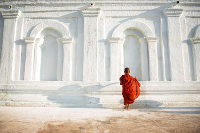 Rear view of monk wearing traditional clothing standing by building