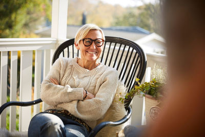 Cheerful mature woman with arms crossed looking away while sitting on porch