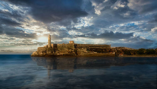 Building by sea against sky during sunset